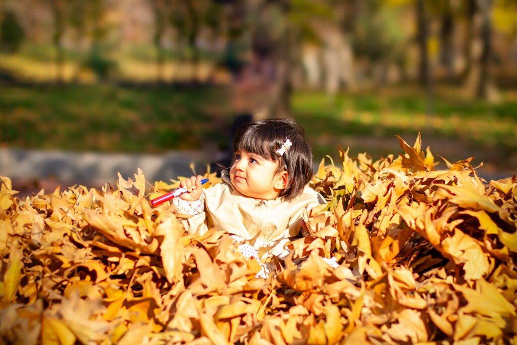A cute child is playing in a pile of leaves.